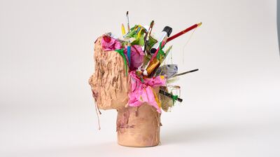 A sculpted head made of clay features art supplies and crumpled pink paper bursting from its top.
