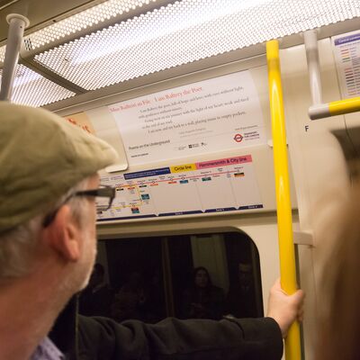 A man in a peaked cap reading a poem on a tube train.
