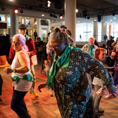 A group of people of all ages are dancing and smiling in the Clore Ballroom