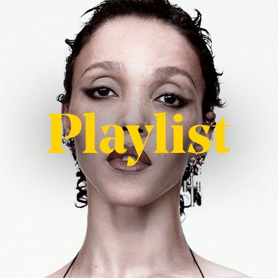 FKA twigs posing in a strappy black top, with dangly silver earrings, and her hand resting on her chest  with 'playlist' overlay