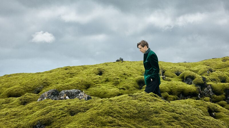Vikingur Ólafsson wearing a green velvet blazer, walking in moss.