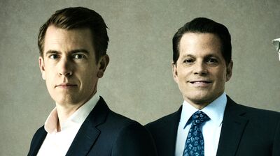 Two men in suits pose between two surveillance cameras directed toward them against a neutral, textured background.