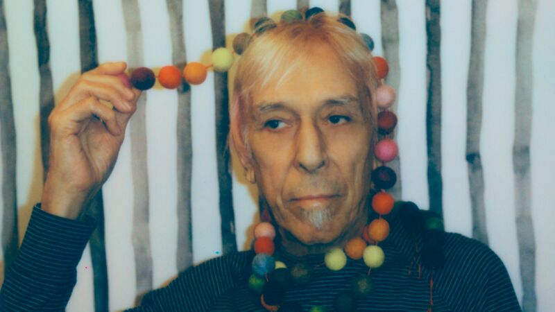 John is wearing a string of coloured balls over his
head and neck, wearing a striped top.