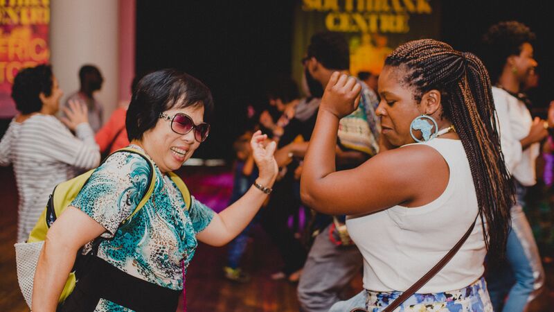 Two people dancing together in the Clore Ballroom at the Southbank Centre, with other people dancing and laughing in the background.