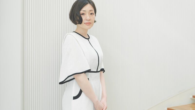 A woman wearing a white dress against a white background, she has short dark hair