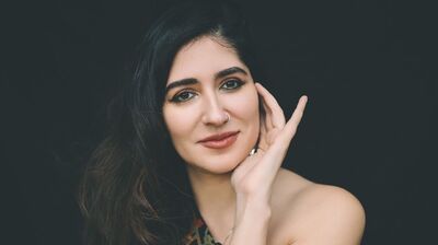 Woman with hand on her jaw looking and facing directly at the camera with a black background behind her.