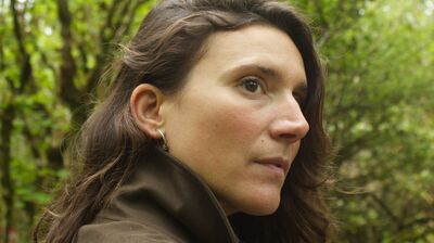 Side profile of a woman looking off camera with green trees behind her