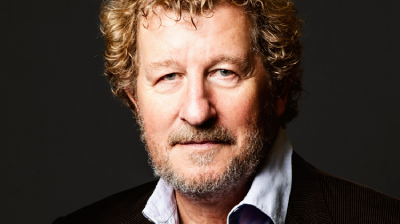 Sebastian Faulks, wearing a black blazer and shirt, looks directorly into the camera with short curly hair.