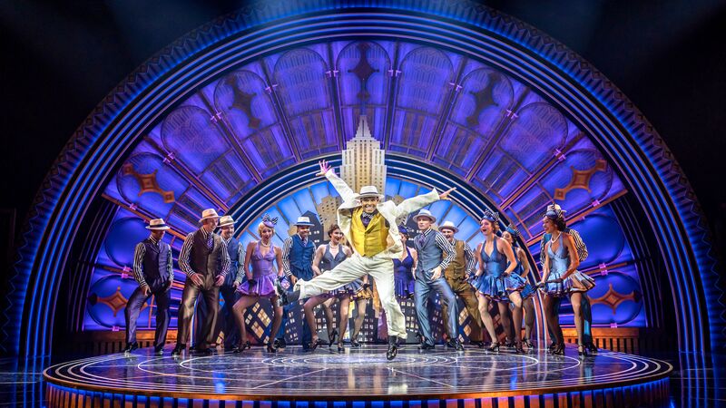 Image shows people dancing on a stage, dressed as though they are living in he 1930s