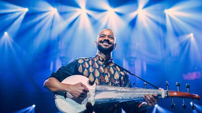 Soumik Datta performing on the Sarod, wearing traditional clothes with blue lights behind him.