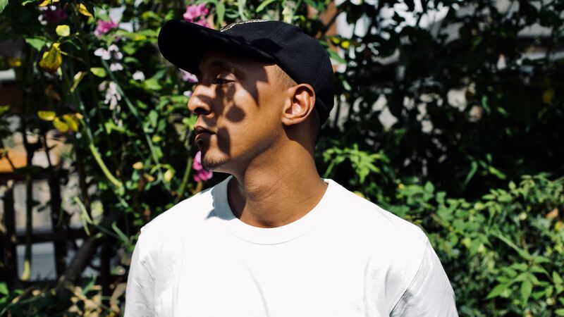 Someone standing under dappled light wearing a white t-shirt and black cap