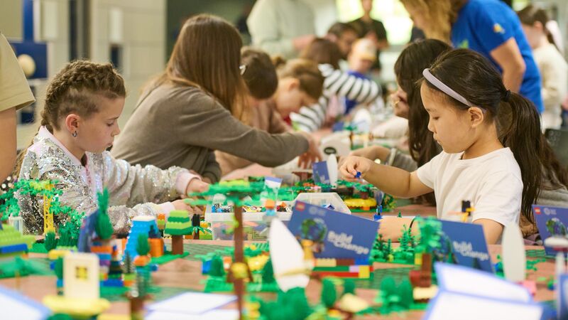 Group of children and adults sitting around a long table playing and building with LEGO