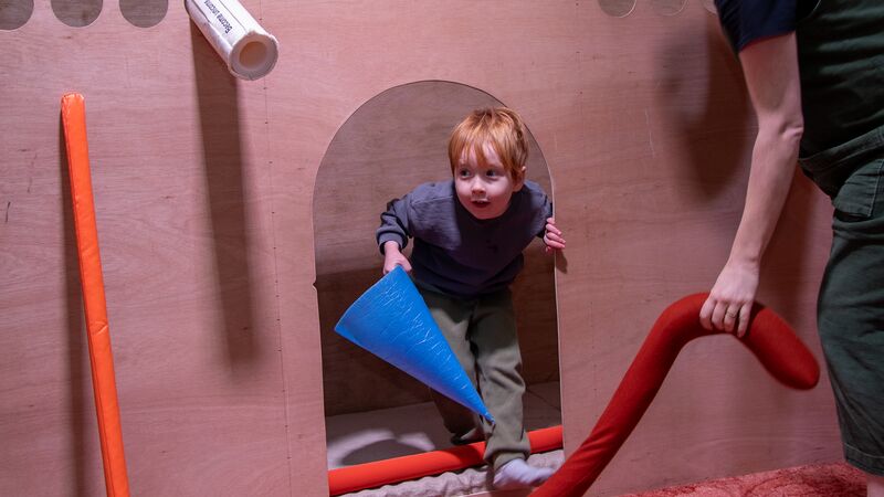 A child is climbing through the recycled playground, holding a large cone and smiling.