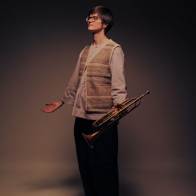 A person holding a trumpet standing with their eyes closed and palms facing up