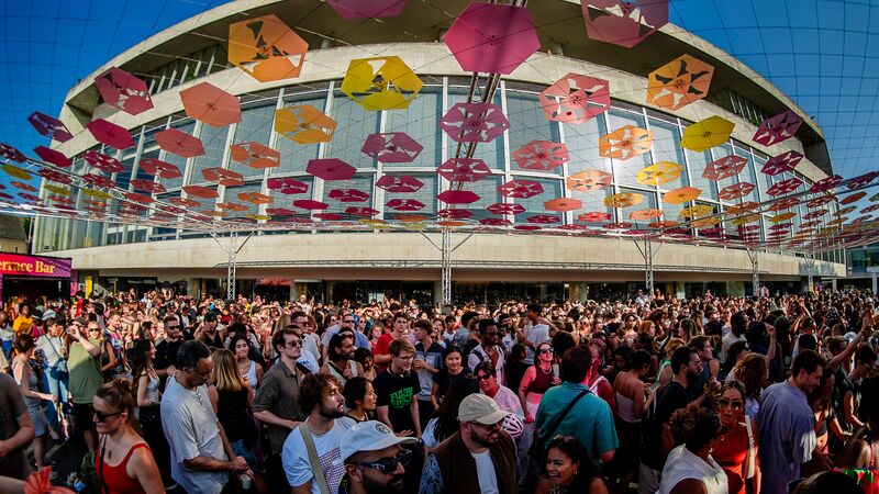 A picture of a crowd of people celebrating on the Southbank Centre Riverside Terrace with pink, yellow and orange bunting overhead