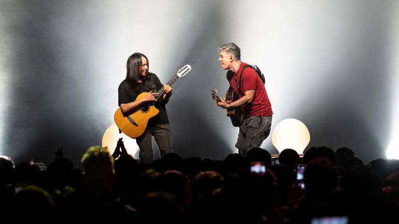 Two people on stage playing guitars and singing, smiling at each other