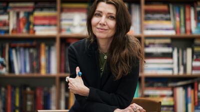 A smiling lady sitting on a chair in front of a full bookcase