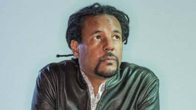 Colson Whitehead wearing a leather jacket against a light blue background.