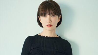 Mieko Kawakami wearing a black dress standing against a pale blue background.