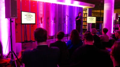 Reader standing on stage in front of an audience at the National Poetry Library.