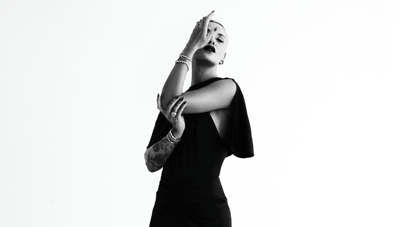 Black and white image of Mariza standing in front of a white backdrop and covering one eye.