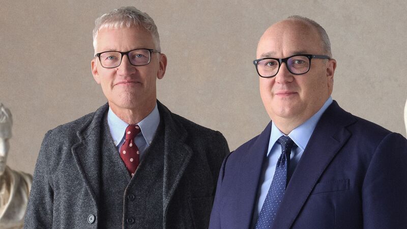 Hosts of The Rest is History standing against a beige background.