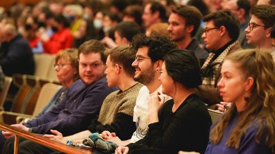 Audience members seated in an auditorium chatting with the people around them