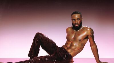 A person wearing sequinned trousers, with lipstick kisses over their chest, posing in front of a pink background