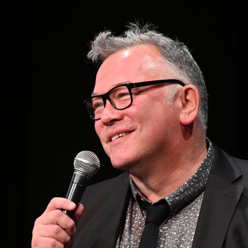 Stewart Lee smiling, holding a mic