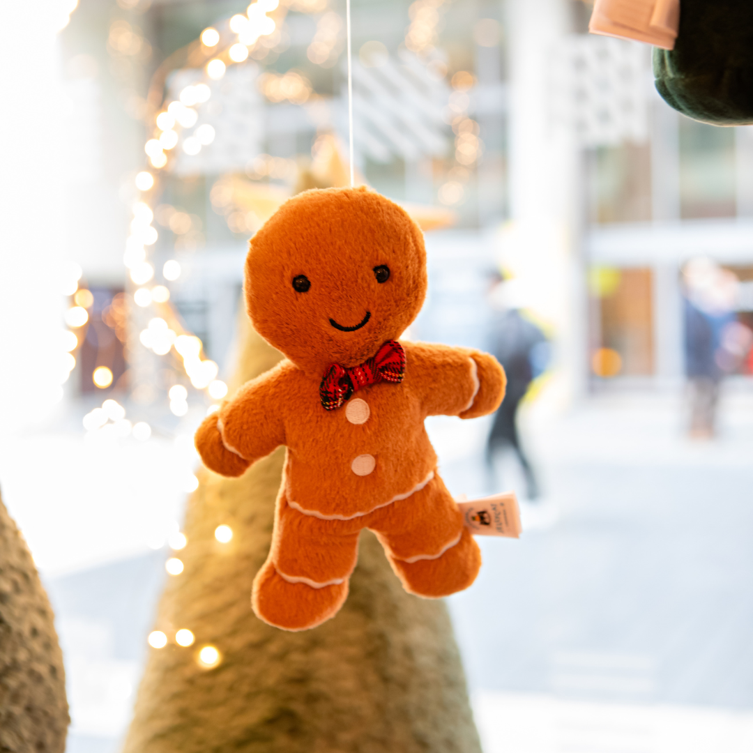 Image of a Jellycat gingerbread man on display in the window of the shop.