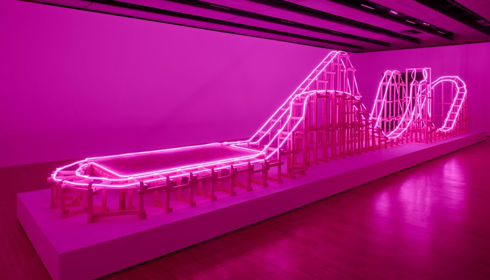 Installation view of large pink sculpture, which is lit up and in the shape of a rollercoaster.
