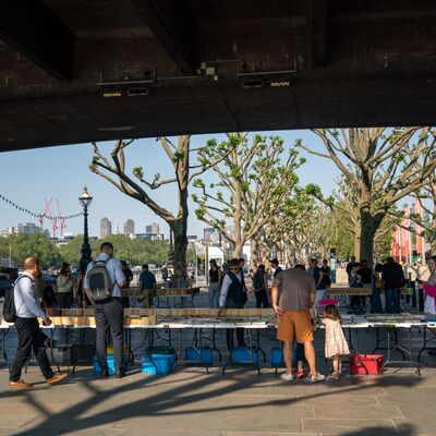 People stand around the tables under a bridge looking at the South Bank Book Market