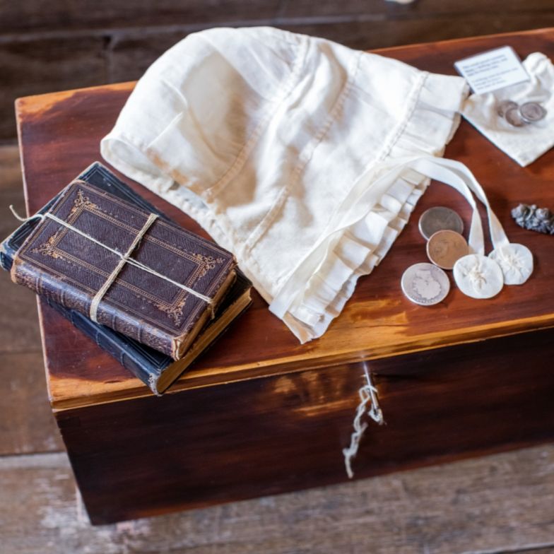 Wooden trunk with a fabric bonnet, books, and coins placed on top of it