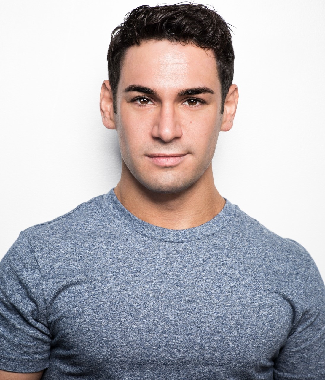 A headshot of Tommy Bracco wearing a blue grey tshirt