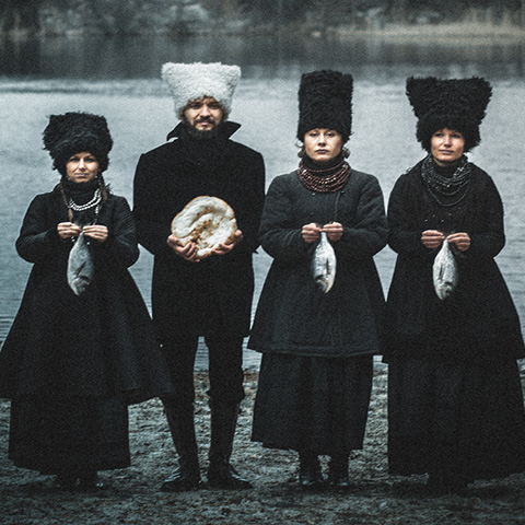 DakhaBrakha members all wearing black and holding either a fish or a bread loaf. 