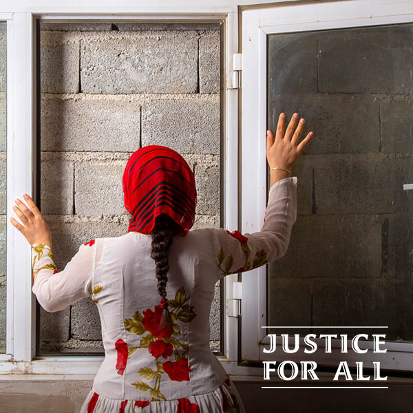 A woman in a white dress and red head scarf staring out a window that has been bricked up.