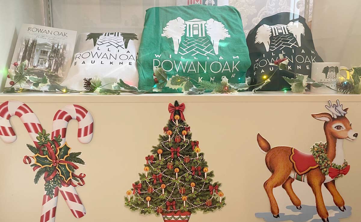 Decorated holiday display case featuring Rowan Oak merchandise: book, tote bag, t-shirt, and coffee cup.
