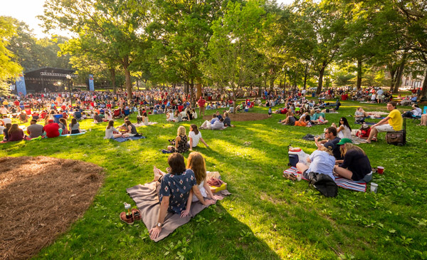 Photo of a crowd at a Summer Sunset Series concert in the Grove at the University of Mississippi. Photo features lots of groups of people sitting on picnic blankets.
