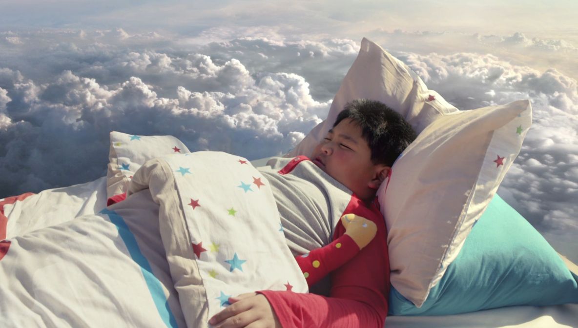 Photo of a boy sleeping in a small bed which floats above the clouds.