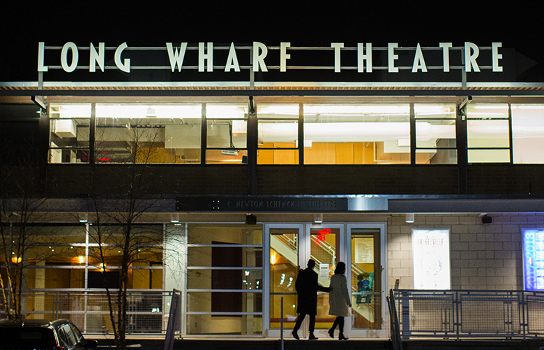 A photo of the exterior of Long Wharf Theatre at night with two patrons entering the front door