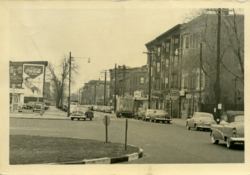 Dixwell Avenue at the intersection of Broadway and Goffe Streets. A large Coca-Cola sign is visible on the left, and several cars are visible on the street.