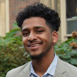 Headshot of a young man with gelled black hair in a coat and shirt