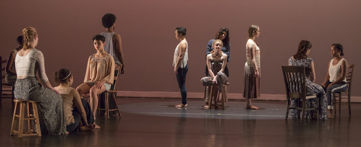 11 performers standing and sitting in formations on a stage