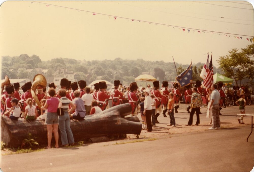 Faded photograph of a marching band and a giant sculpted log on a street